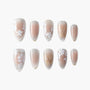 Handmade press-on nails with nude base, white floral designs and gold accents, arranged on white background.