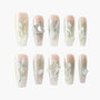 Handmade press-on nails with 3D white floral designs, pearls, crystals, and nude glitter base.