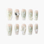 Handmade press-on nails with floral designs, gems, pearls, and soft nude-green gradient.