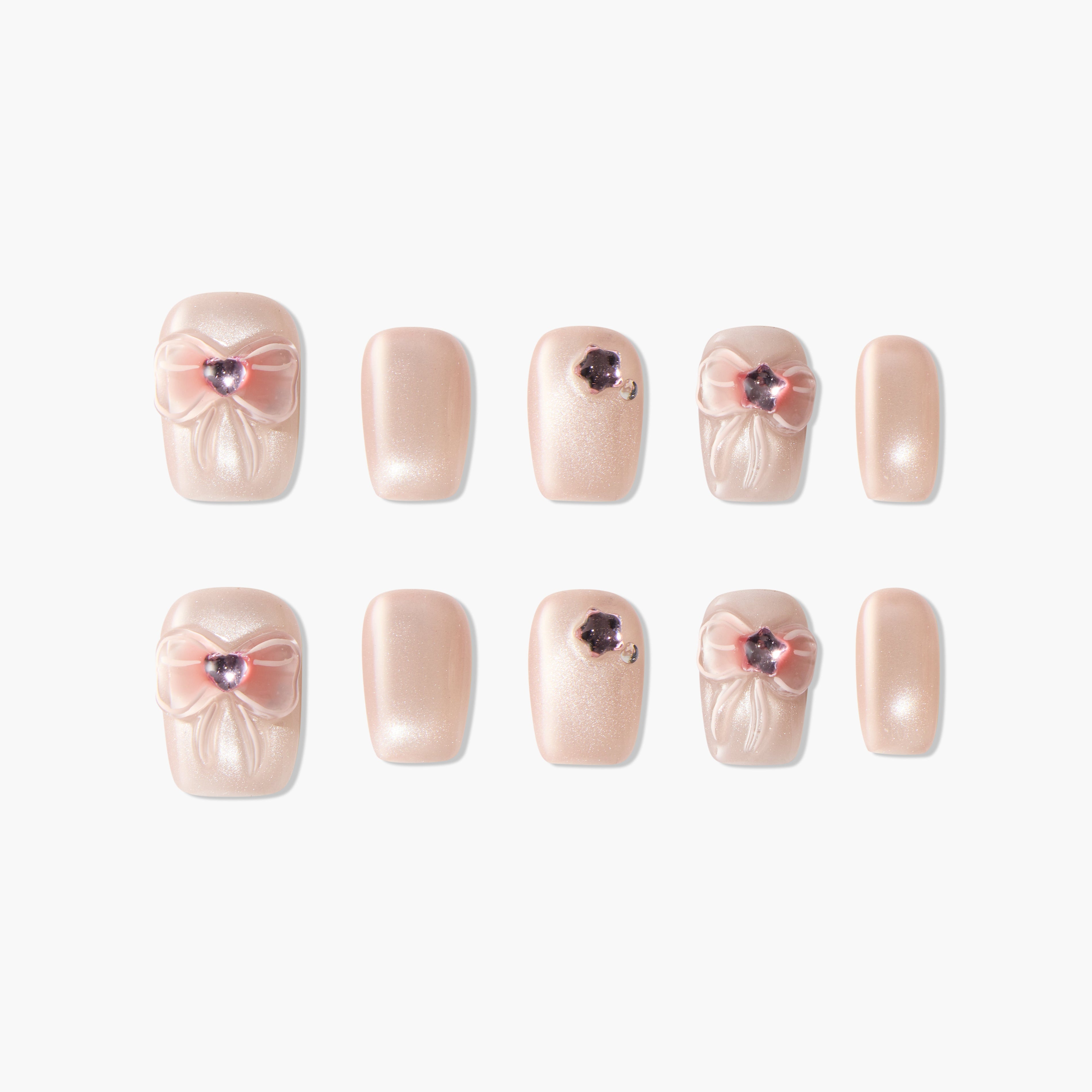 Handmade press-on nails in shimmery nude with pink 3D bows and rhinestone accents