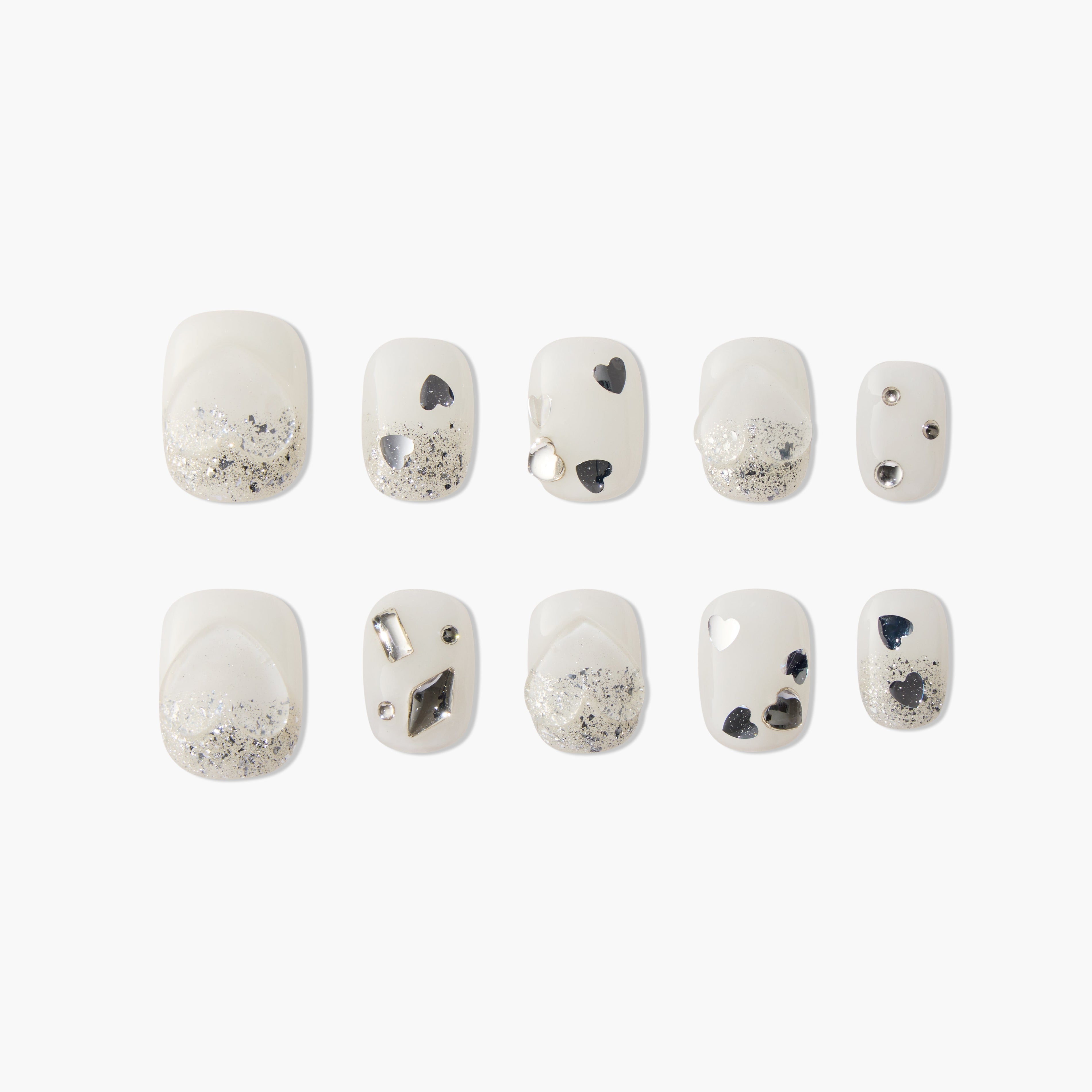 White press-on nails with silver glitter, black heart accents, and metallic embellishments