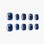 Set of blue glitter press-on nails with heart and swirl designs, displayed on white background.