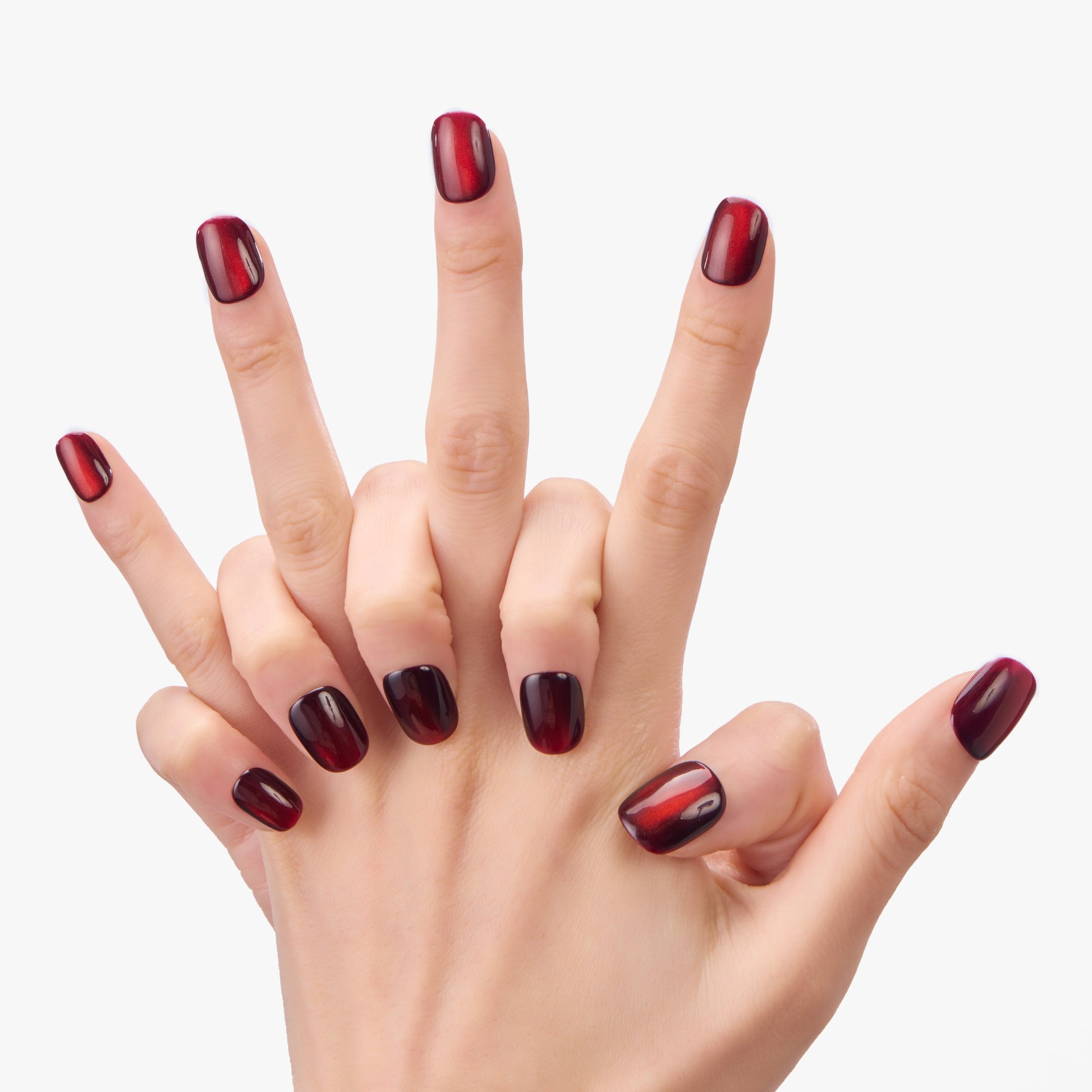 Hand with glossy burgundy press-on nails, short almond shape, on a white background.