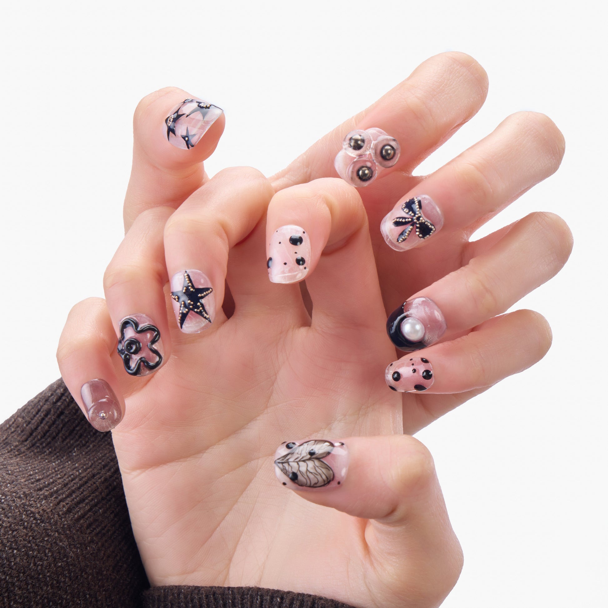 Hand with premium handmade press-on nails featuring black floral, star, bow, pearl, and dot designs