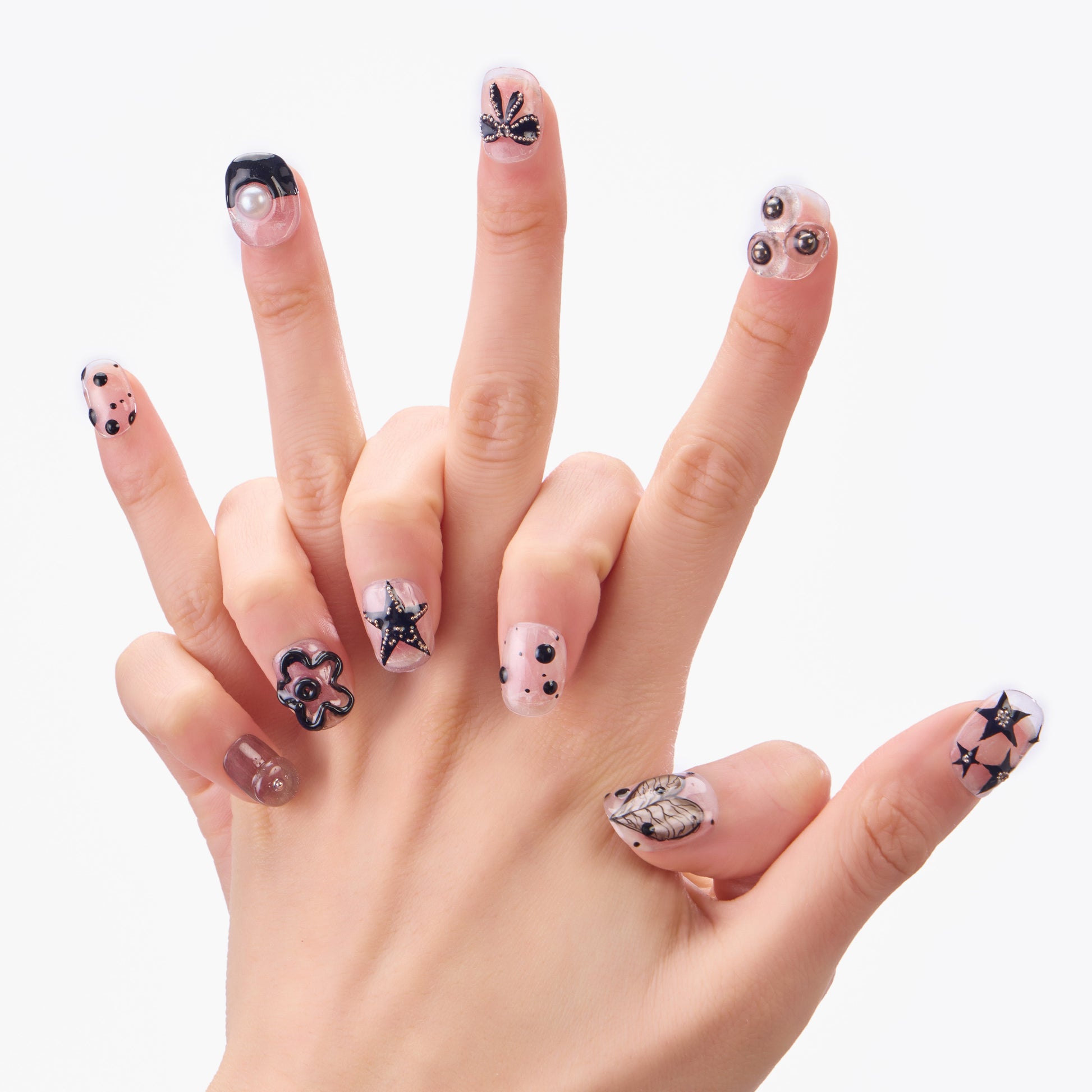 Hand with reusable press-on nails in black and nude, featuring 3D stars, flowers, and pearls.