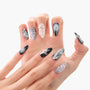 Hand with long stiletto press-on nails in metallic silver and black, 3D bows and rhinestones