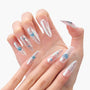 Hand with long press-on nails, clear with silver foil and blue heart-shaped accents.