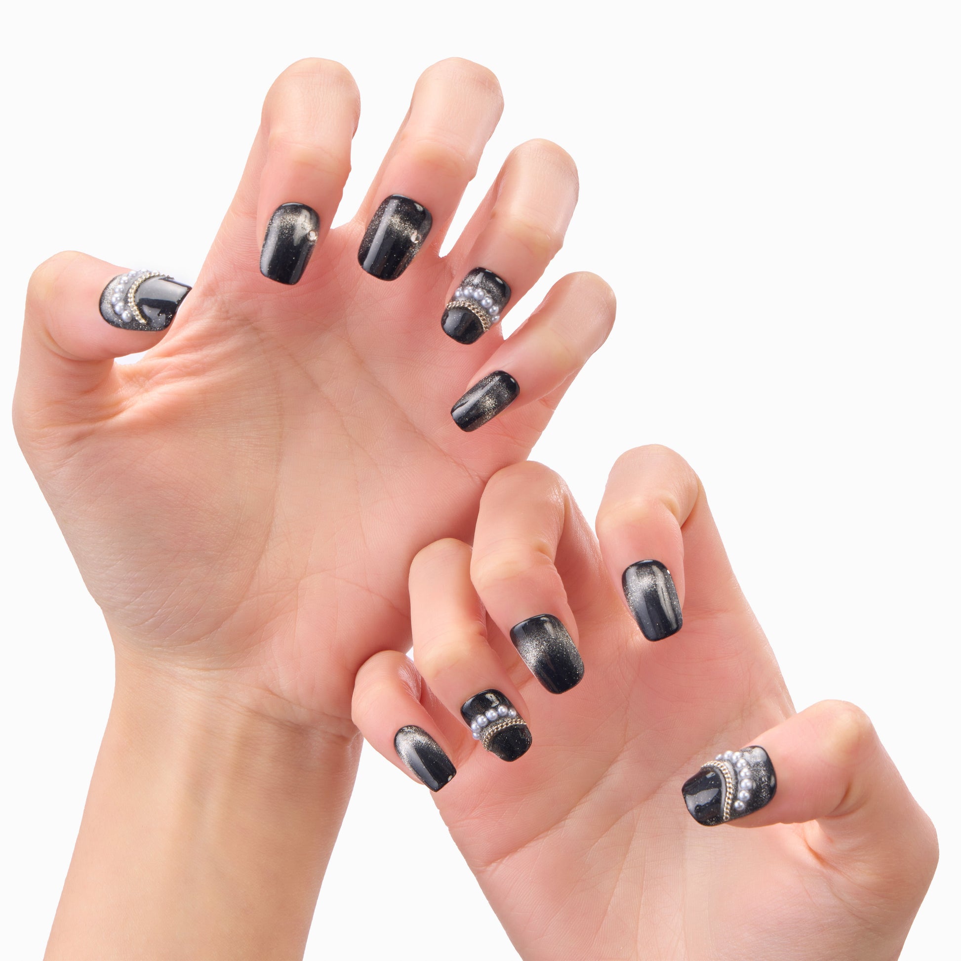 Hands with black and silver press-on nails featuring rhinestone and metallic accents