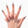 Hand with long almond-shaped press-on nails featuring marble design and rhinestone accents