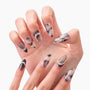 Hand with long almond press-on nails in marbled black, white, and gold design with rhinestones.