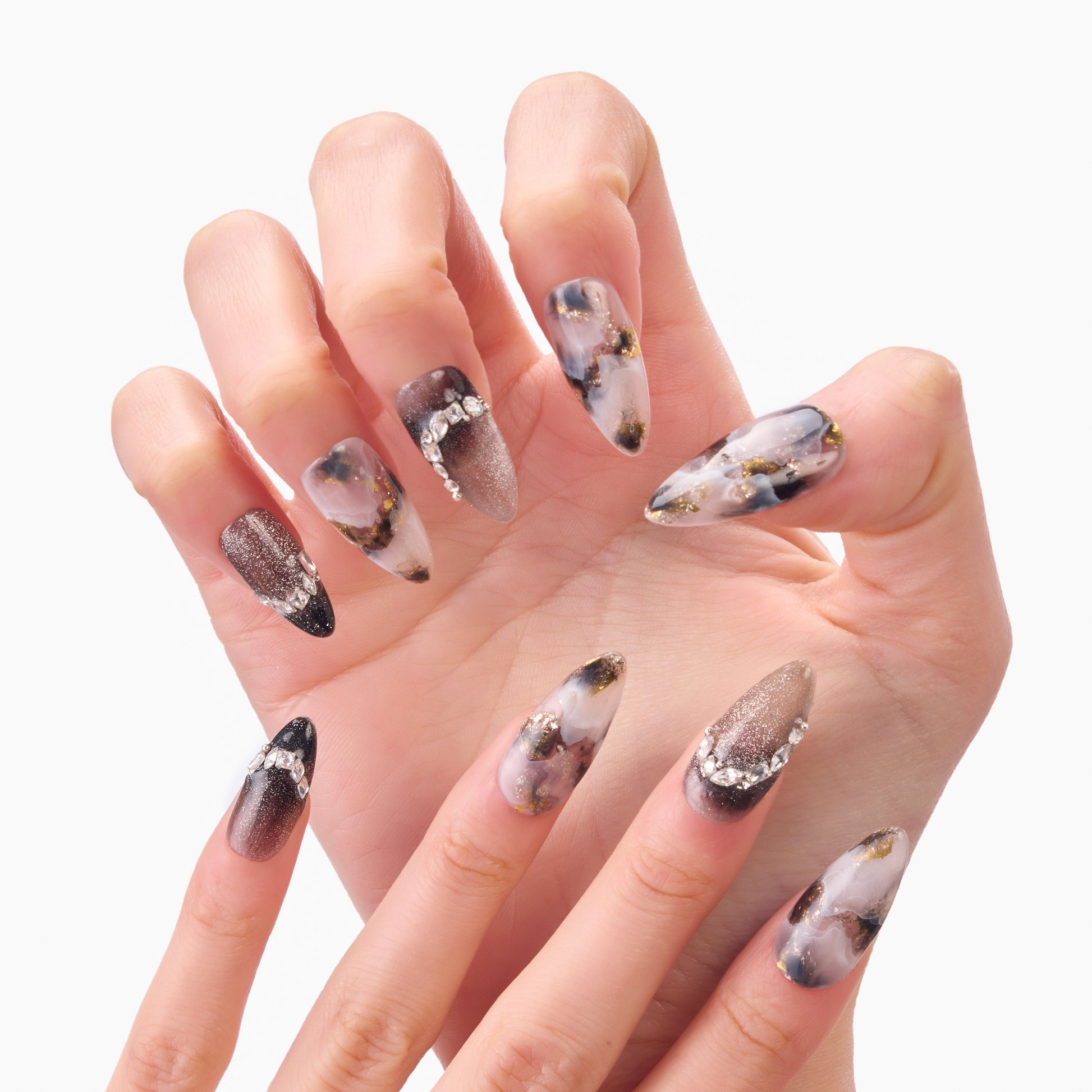 Hand with long almond press-on nails in marbled black, white, and gold design with rhinestones.