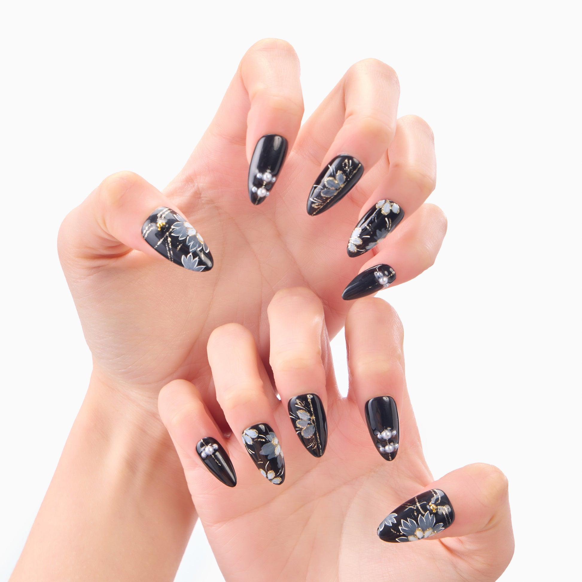 Black floral press-on nails with pearl accents displayed on hands, almond shape, elegant design