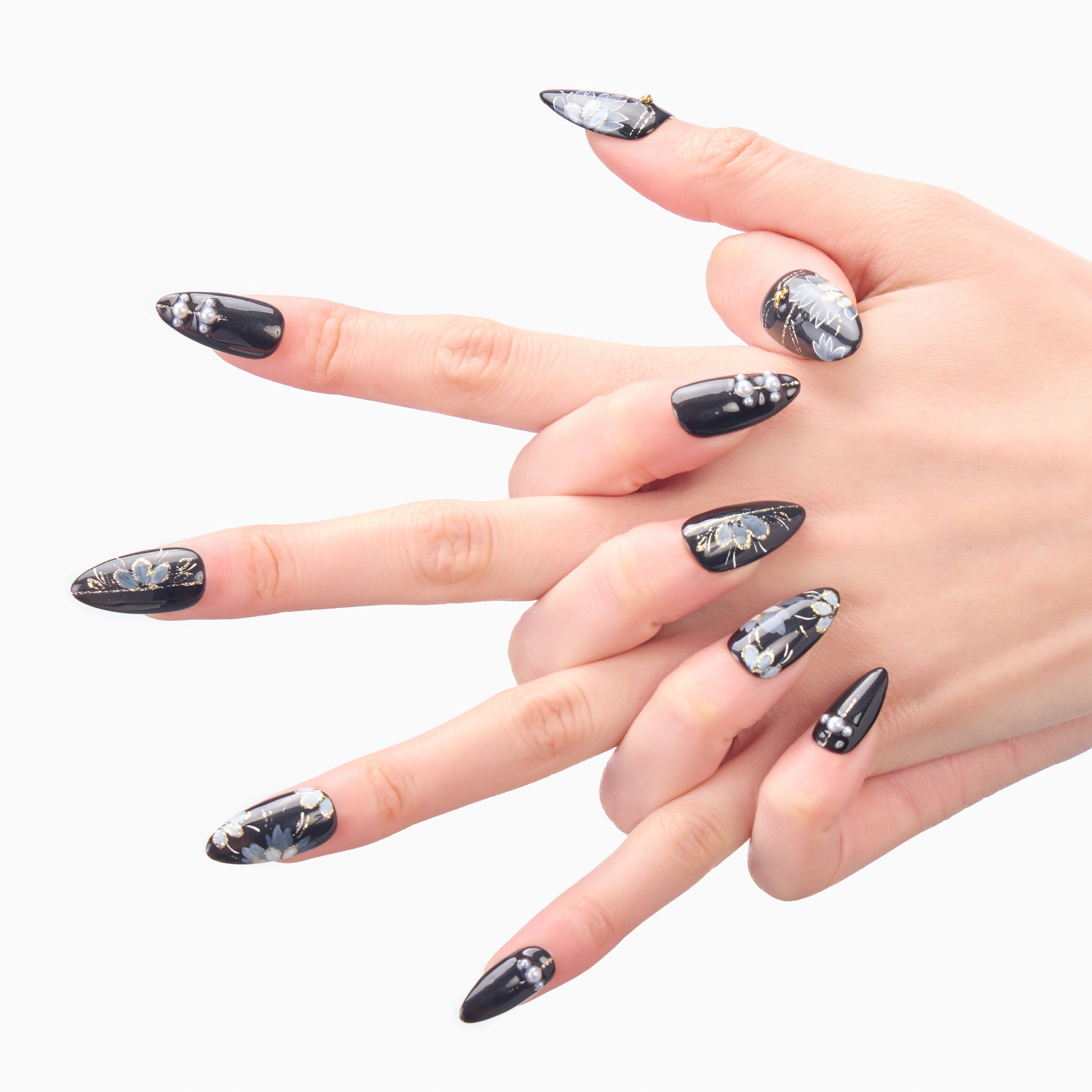 Hand with black press-on nails featuring floral and gemstone nail art on a white background