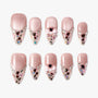 Pink press-on nails with glitter, rhinestones, heart gems, and 3D bows on a white background.