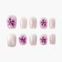 Handmade press-on nails with shimmery pink base and 3D purple flower accents, arranged on white background