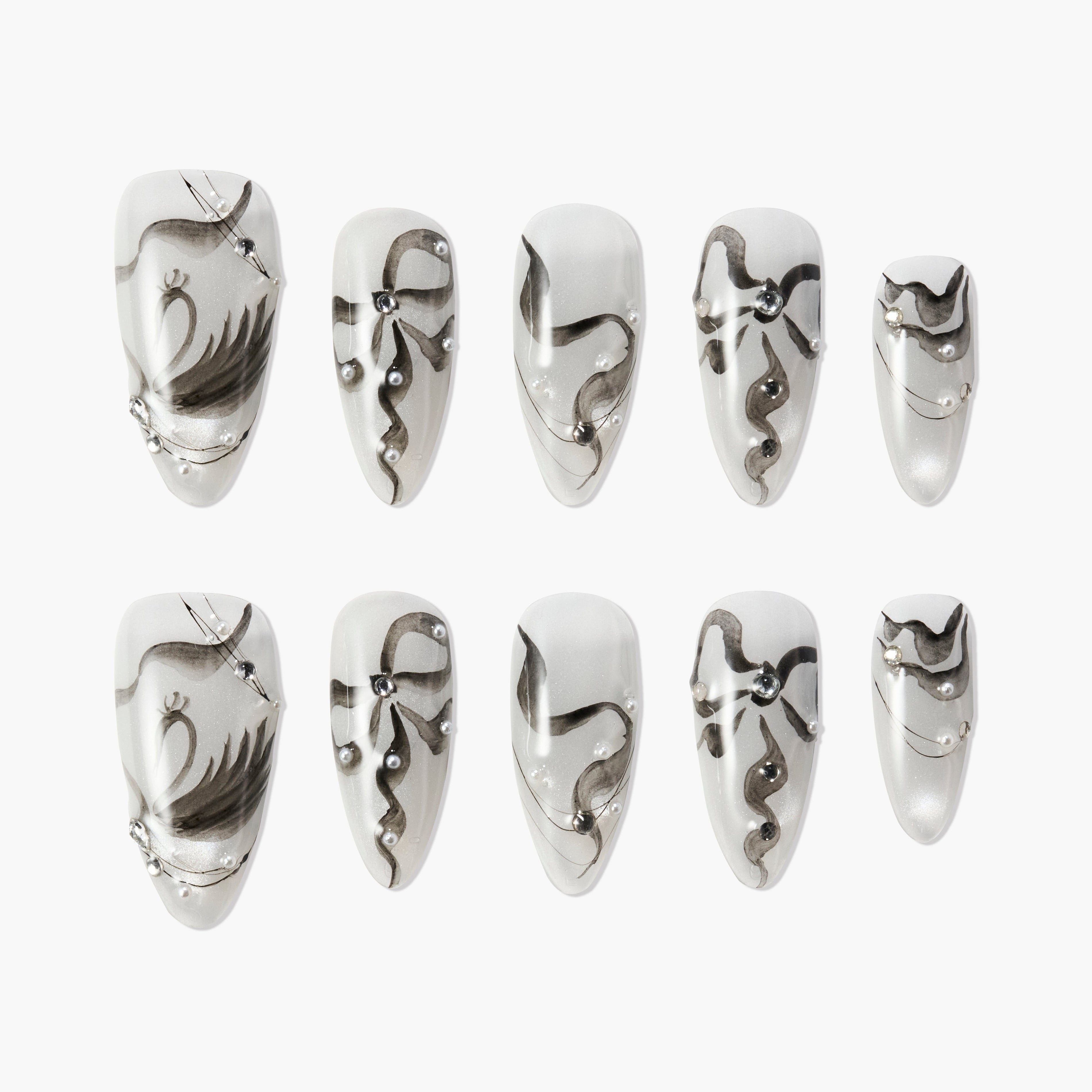 Handmade press-on nails with black abstract designs and pearl accents on a white base.