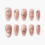 Shimmery nude press-on nails with peach accents and rhinestone embellishments