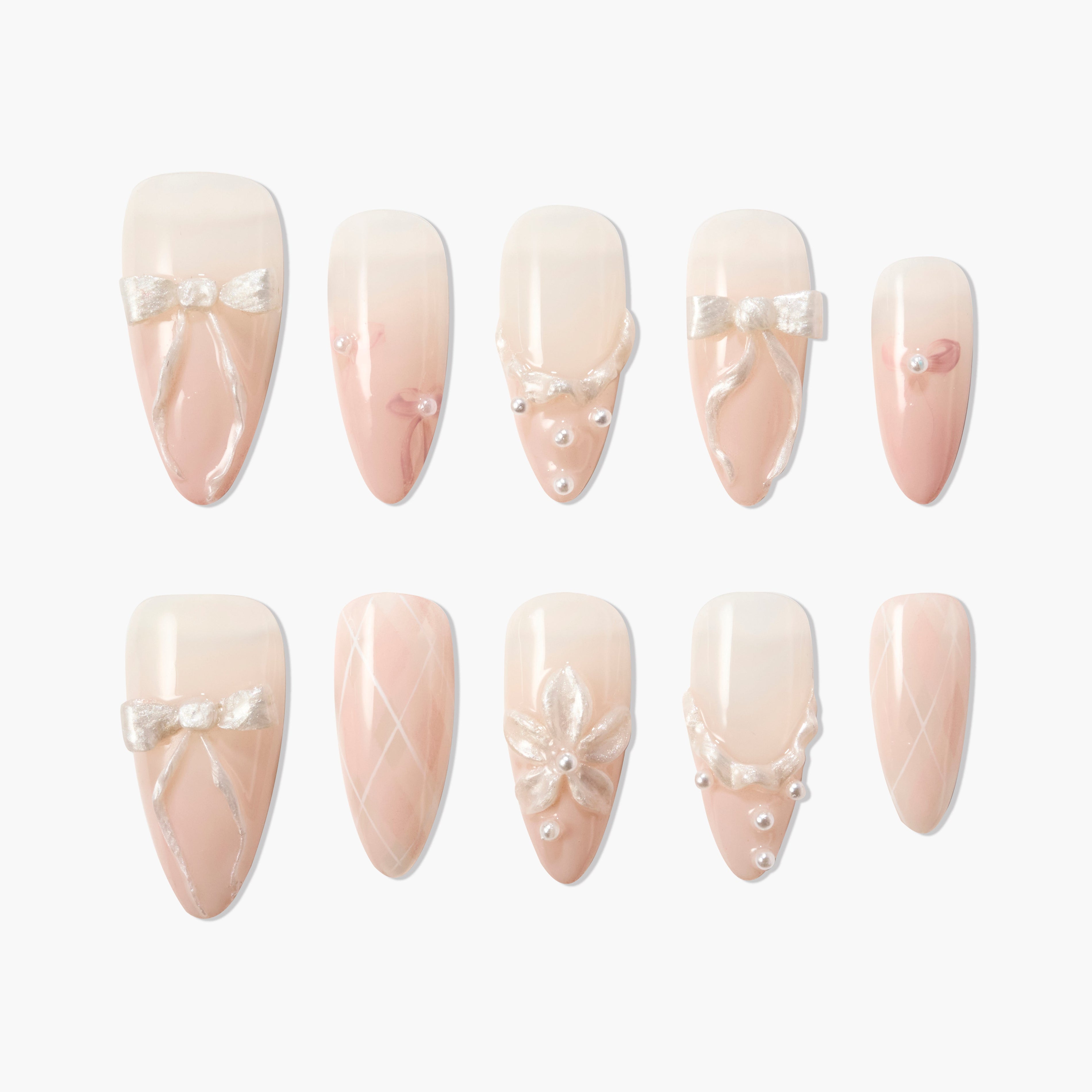 Handmade press-on nails in nude pink with bow, pearl, and flower 3D designs on white background.