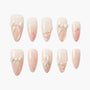 Handmade press-on nails in nude pink with bow, pearl, and flower 3D designs on white background.