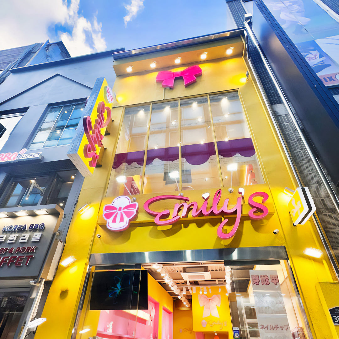 Bright yellow storefront with pink signage and large glass windows, showcasing a press-on nail shop.