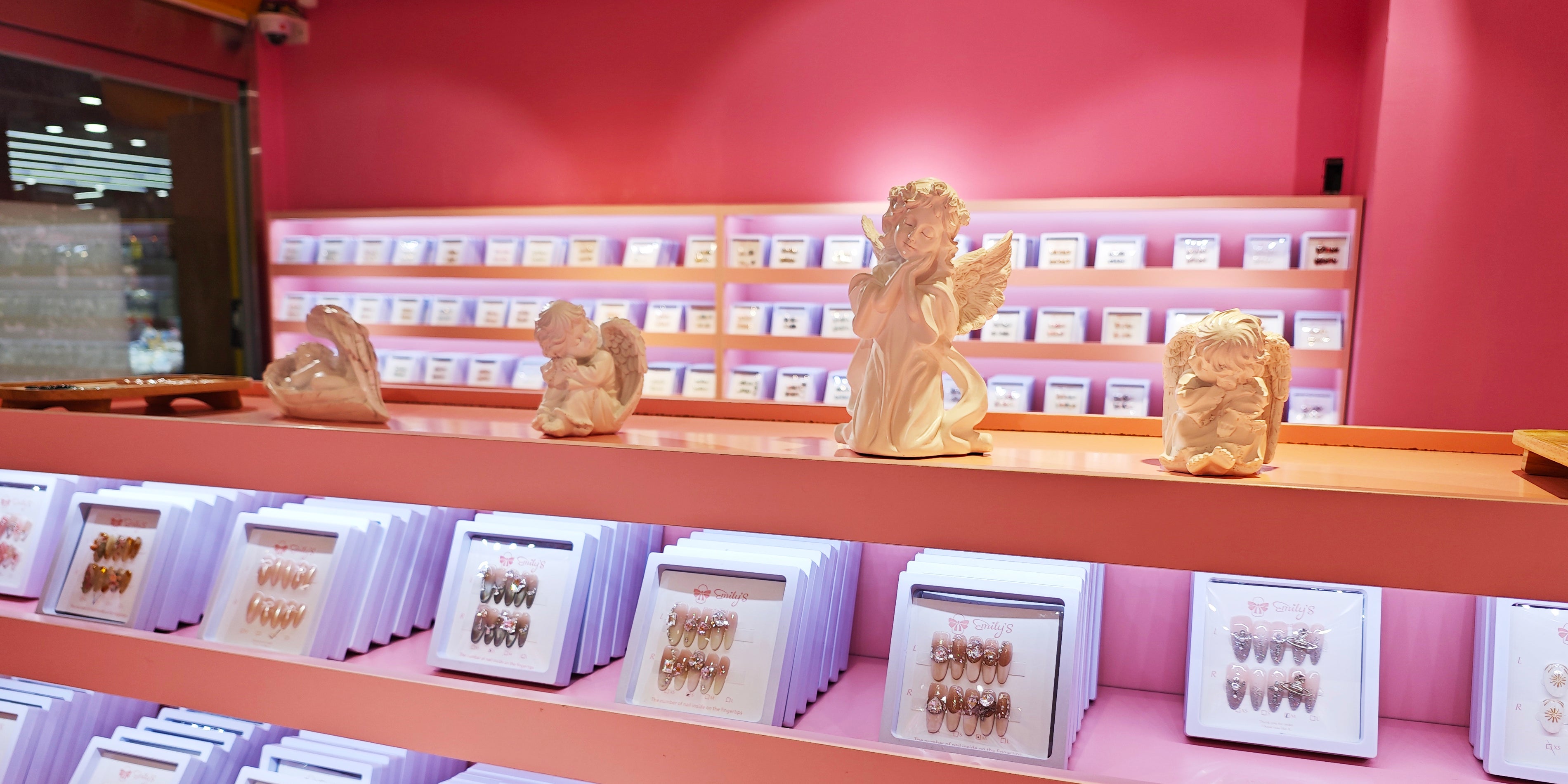 Handmade press-on nail display with angel figurines in a pink boutique setting