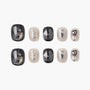 Handmade press-on nails with black and beige gothic designs, metallic wing, heart, and sword accents.
