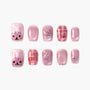 Handmade pink press-on nails with glitter, plaid, heart, and cute face designs on white background.