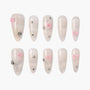 Handmade press-on nails with pale glitter, pink bows, and rhinestone accents, arranged in two rows