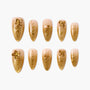 Gold floral press-on nails with 3D flower designs on nude gradient background, arranged in two rows.