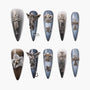 Handmade press-on nails in blue and gray ombre with 3D metallic cross, angel, and fleur-de-lis charms
