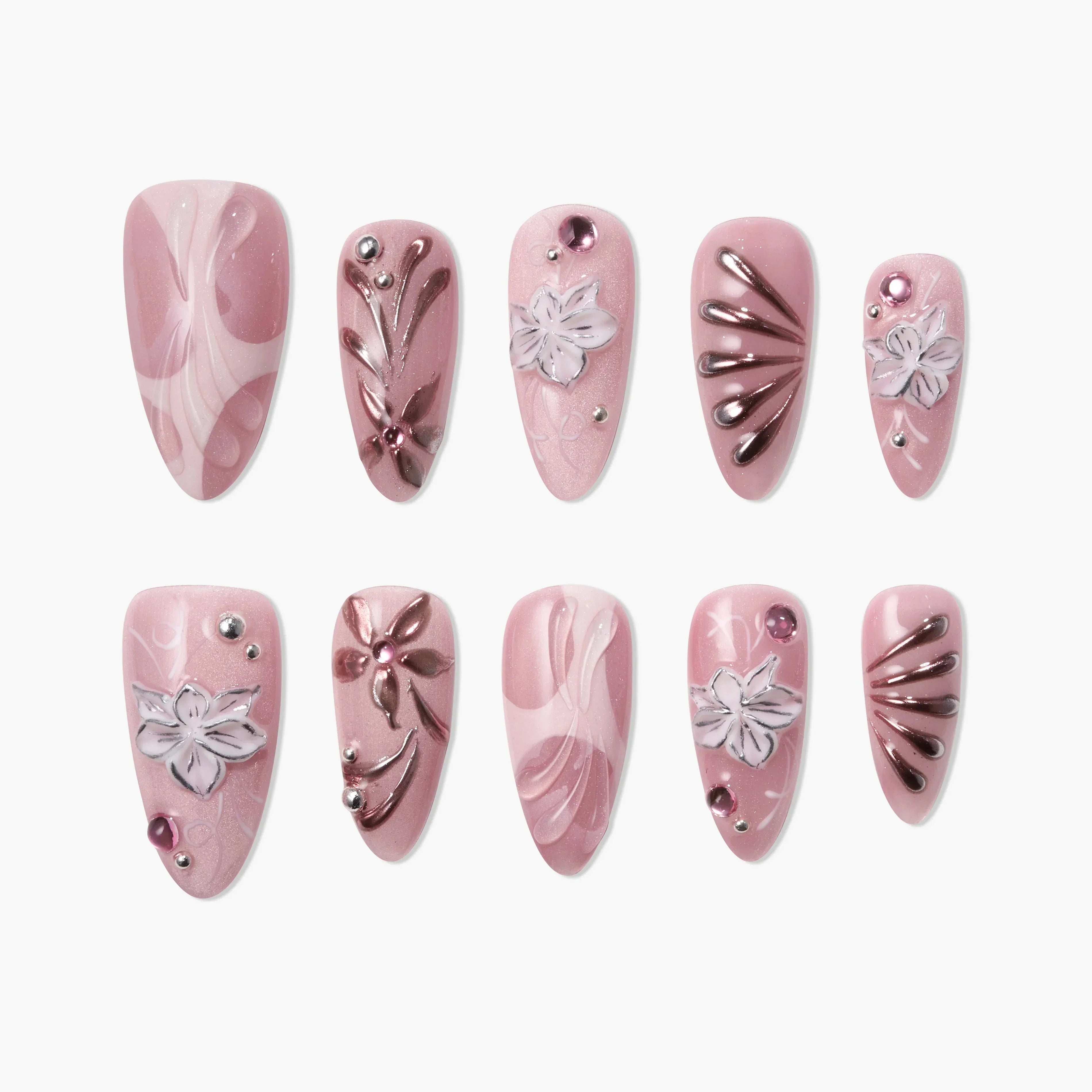 Pink press-on nails with white flower accents, metallic details, and rhinestone embellishments.