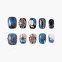Celestial-themed press-on nails with blue glitter, gold sun and star designs, and colorful gems
