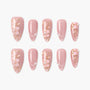 Pink press-on nails with floral designs, gold accents, and pearl embellishments.