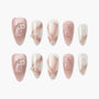 Pink and white press-on nails set with pearl accents, glitter, and gold ribbon details.