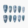Handmade blue press-on nails with 3D floral designs, silver accents, and rhinestones on white background
