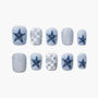 Handmade press-on nails with blue star, checkered, and cartoon heart designs on a white background