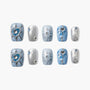 Blue and silver press-on nails with heart, gem, and starburst designs, arranged on white.