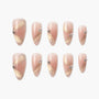 Almond-shaped press-on nails in pink with gold diagonal accents and pearl rhinestone details.