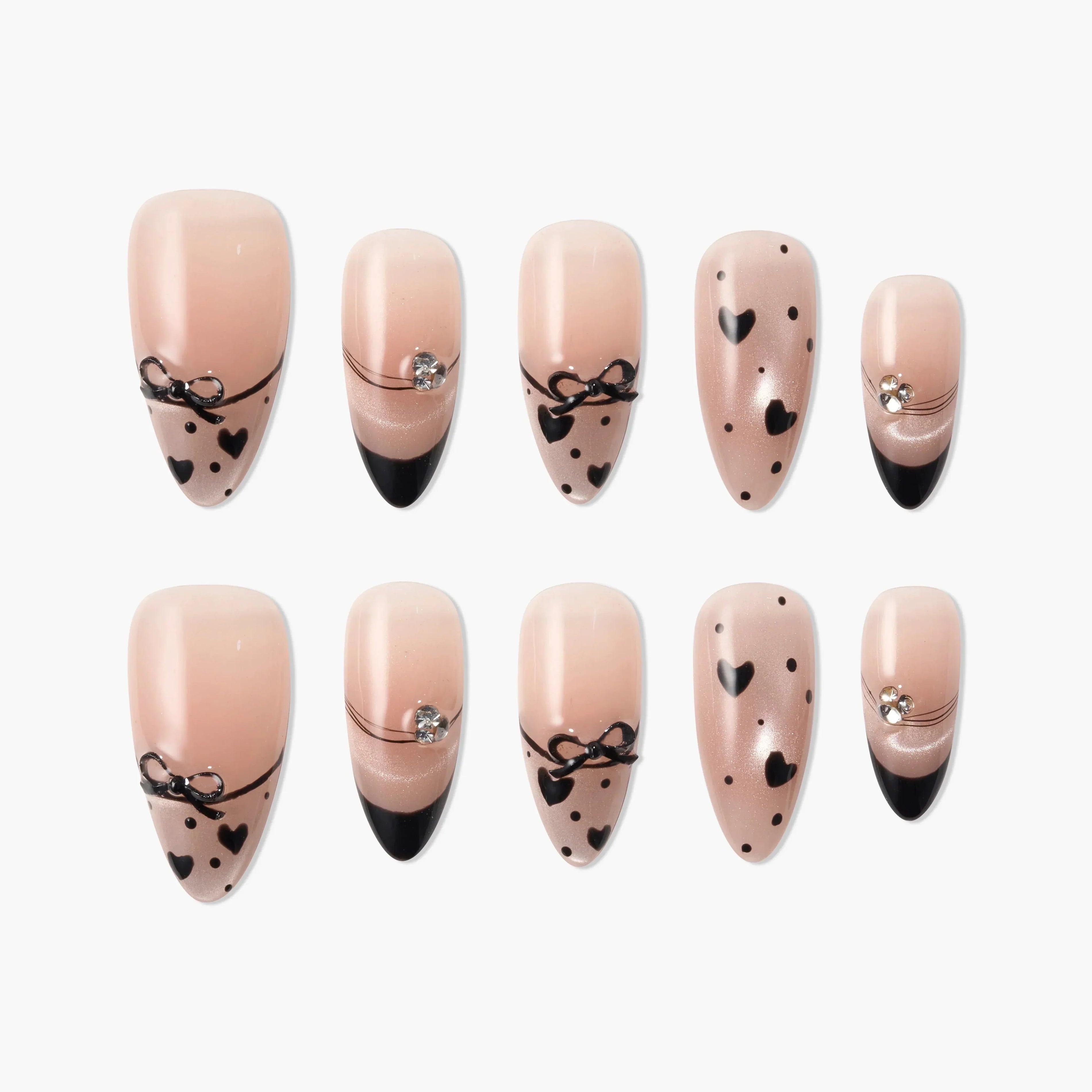 Handmade press-on nails with nude base, black hearts, bows, and rhinestone accents, displayed on white background.