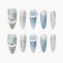 Blue and white press-on nails with 3D floral designs, pearls, bows, and jeweled accents.