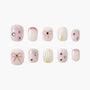 Pink and white press-on nails with bow accents, rhinestones, and swirl designs