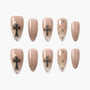 Nude press-on nails with metallic cross charms, rhinestones, and glitter accents, stiletto shape