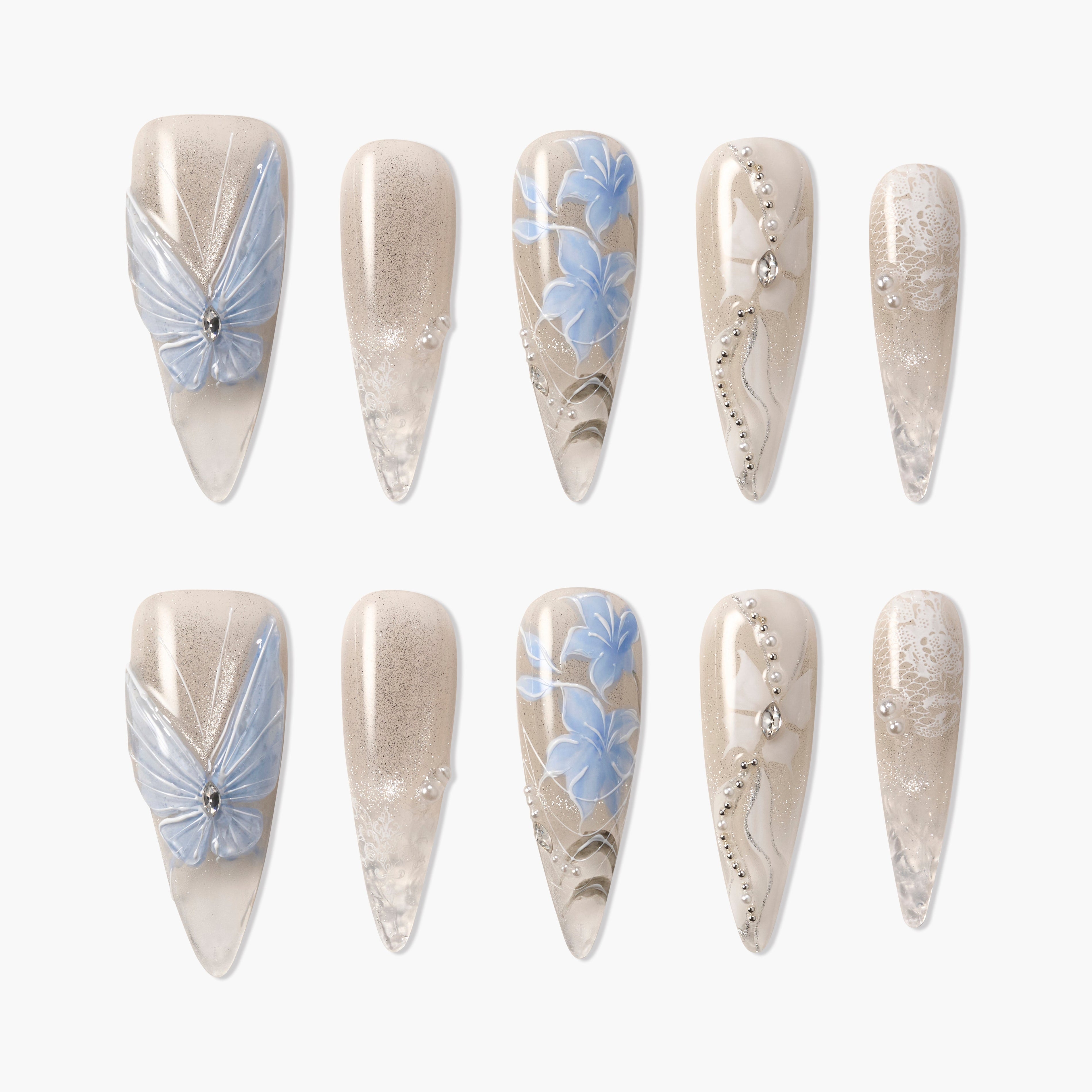 Long almond press-on nails with nude base, blue floral patterns, silver rhinestones, and butterfly accents