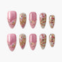 Handmade press-on nails with pink glitter, 3D floral accents, and gold floral designs.