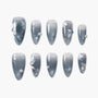 Gray press-on nails with white floral designs, pearl and gem accents, glossy finish