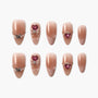 Handmade nude press-on nails with pearl, butterfly, bow, and heart gem embellishments.