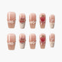 Handmade pink press-on nails with 3D strawberry, floral, pearl, and bow designs on white background