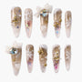 Gold and white winter press-on nails with snowflakes, glitter, bows, and 3D Christmas tree accents.
