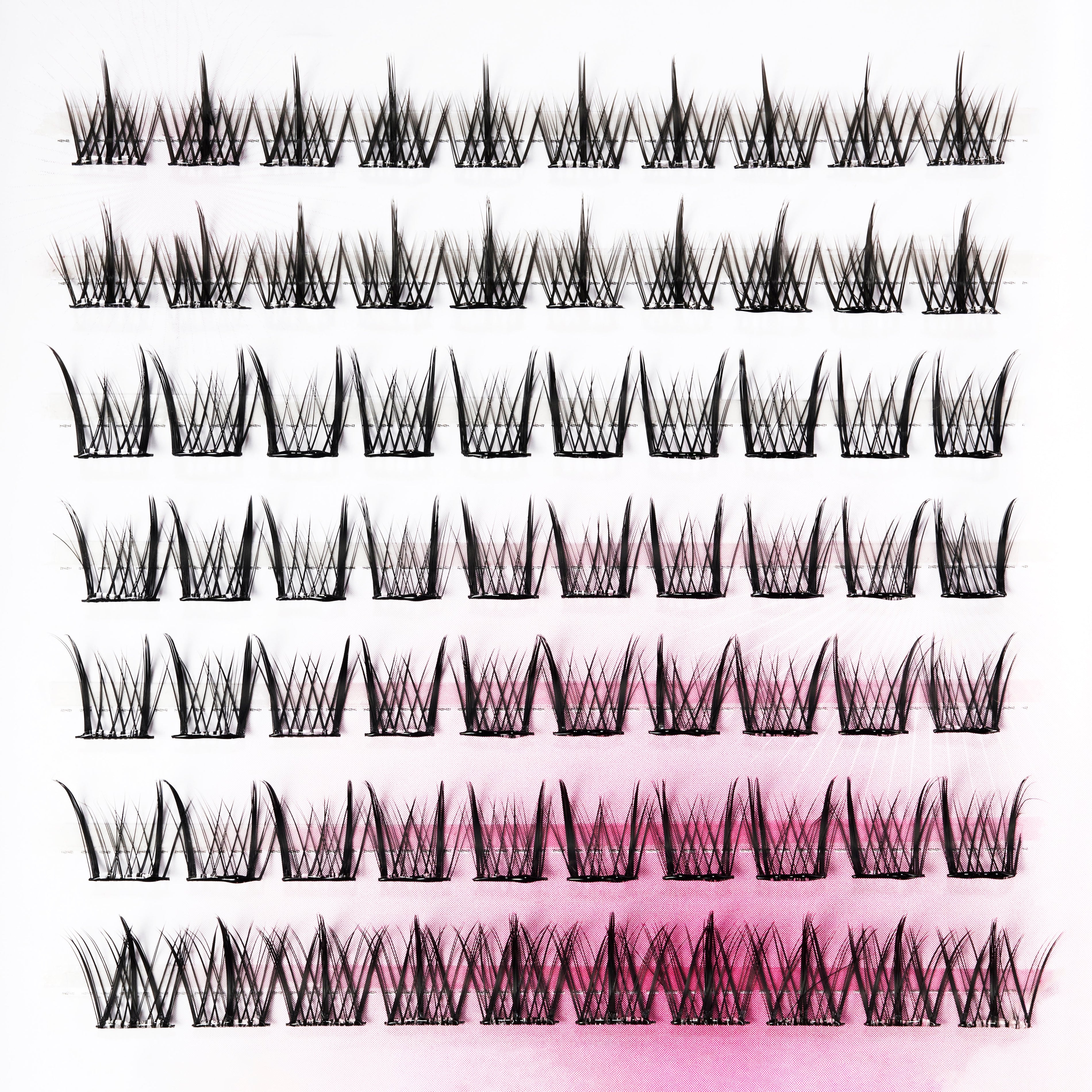 Multiple rows of handmade false eyelash clusters displayed on a white and pink background.