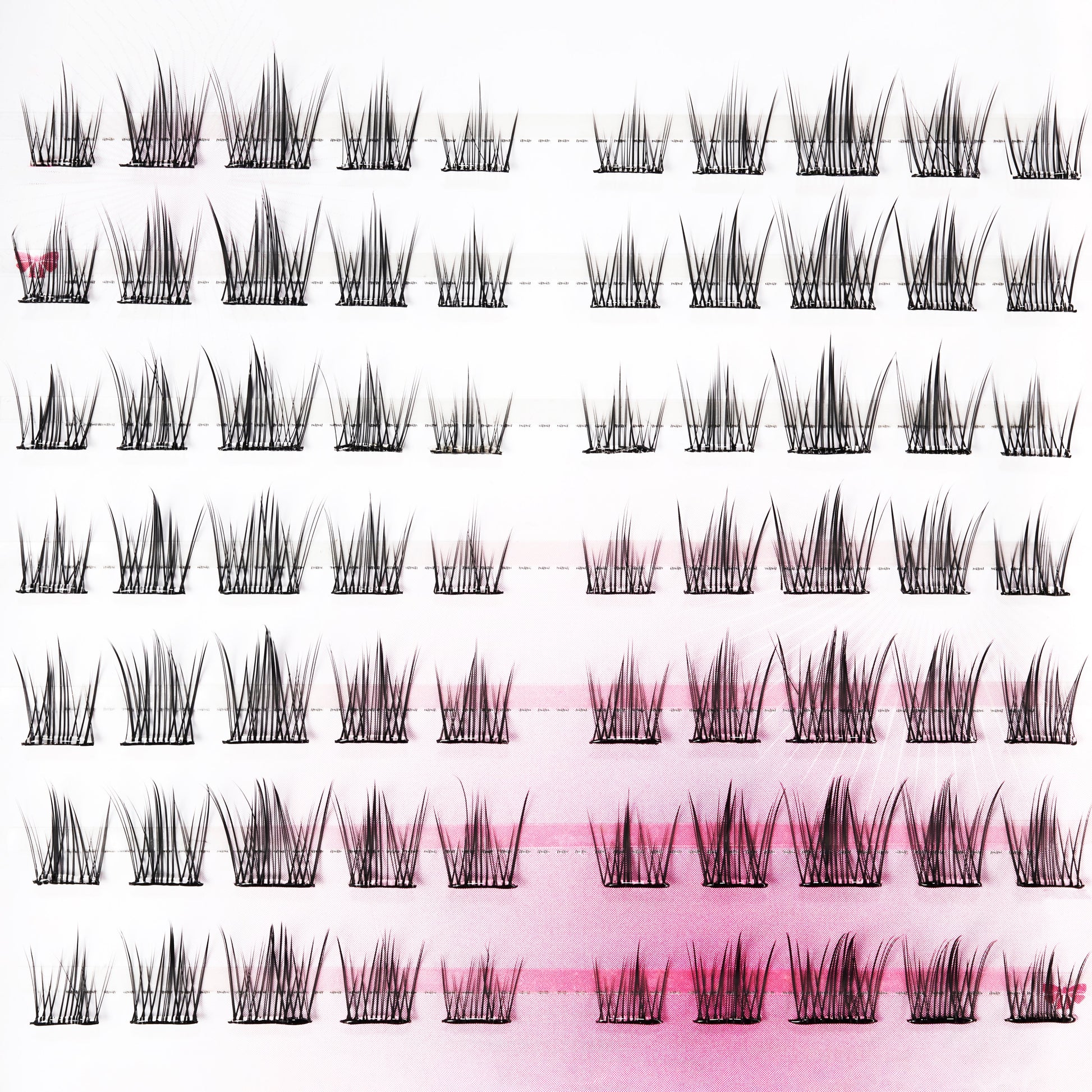 Handmade false eyelash clusters arranged in rows on a pink and white background.